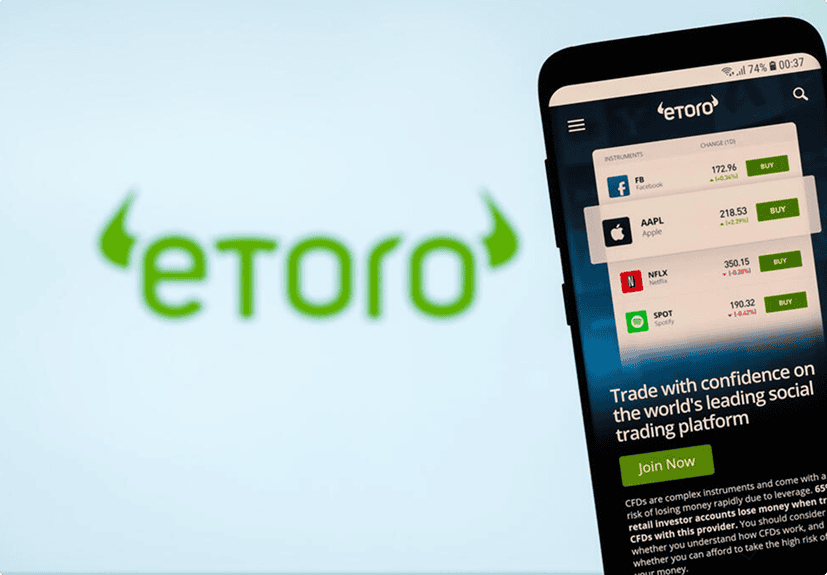 A smartphone displays the eToro trading app interface with stock prices in front of a blurred eToro logo in the background.