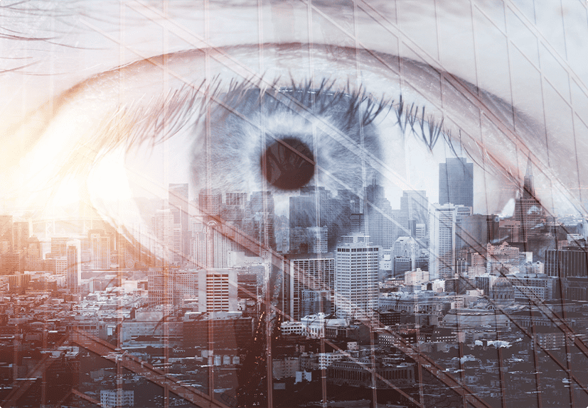 A large, blue human eye is superimposed over a cityscape, blending the patterns of the eye with the buildings below.